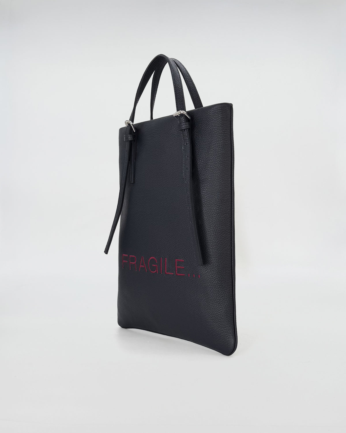 Black leather handbag with 'FRAGILE...' embroidered in red, designed for work and versatile use.
