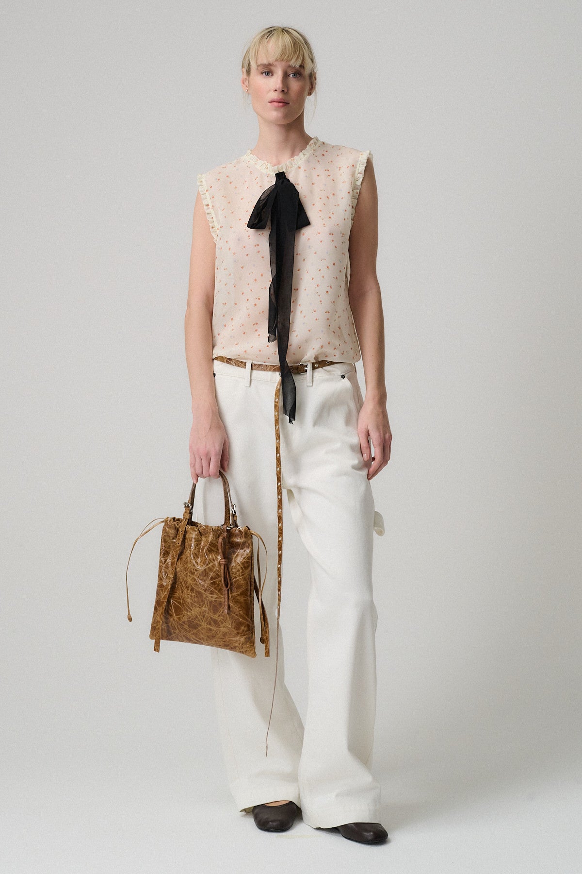 Top LULU SETA FANTASIA ROSE indossato da una modella con pantaloni bianchi e borsa marrone.