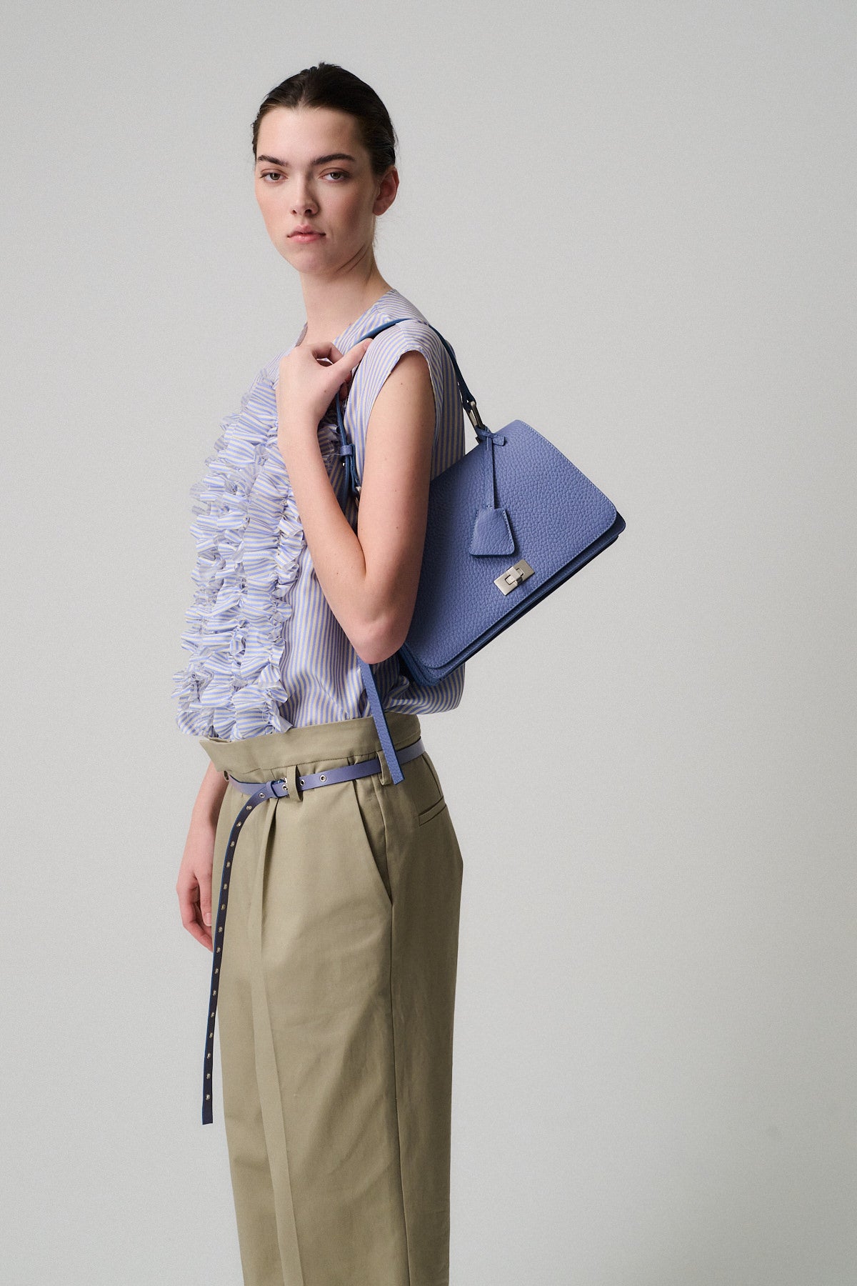 Modella con blusa a volant e borsa QUEEN VITELLO blu a spalla in un ambiente neutro.