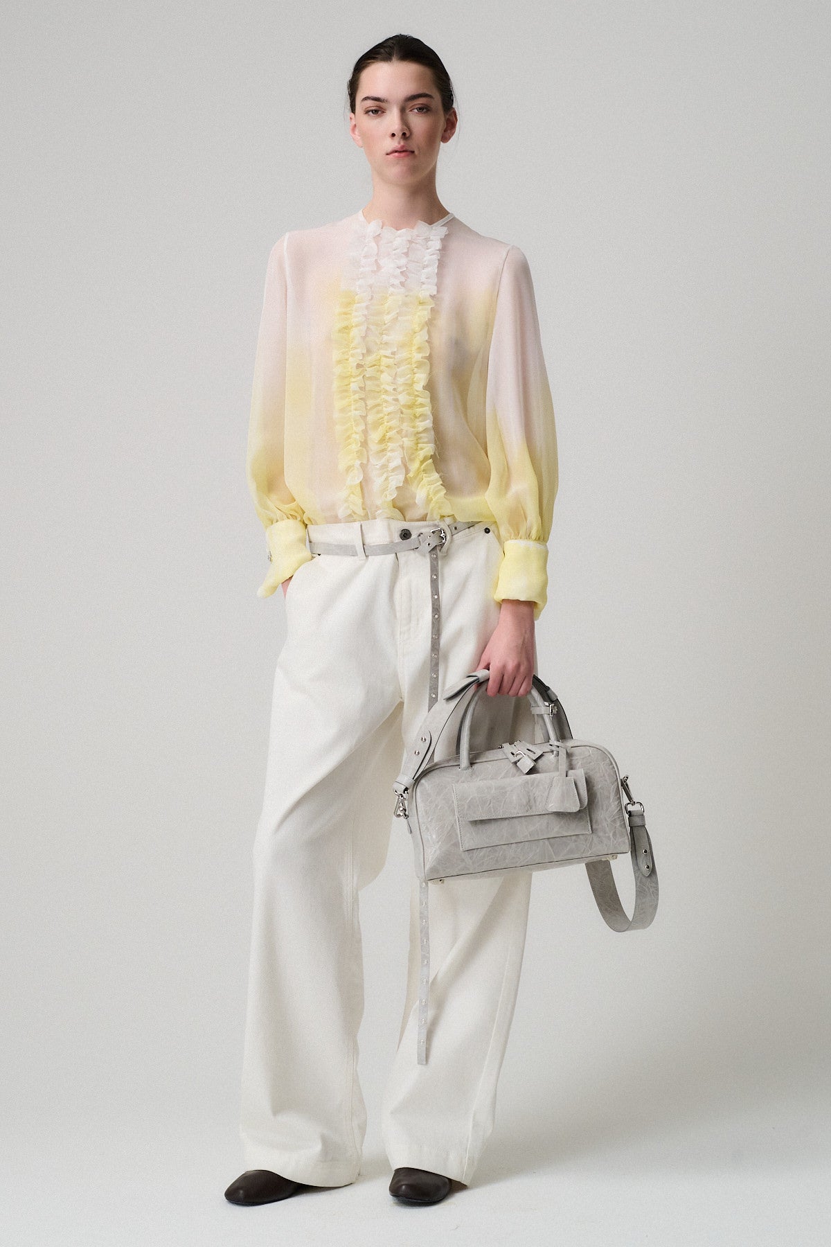 Modella che indossa una camicia gialla trasparente e pantaloni bianchi, con una borsa ZOE SMALL VITELLO STRIZZATO.