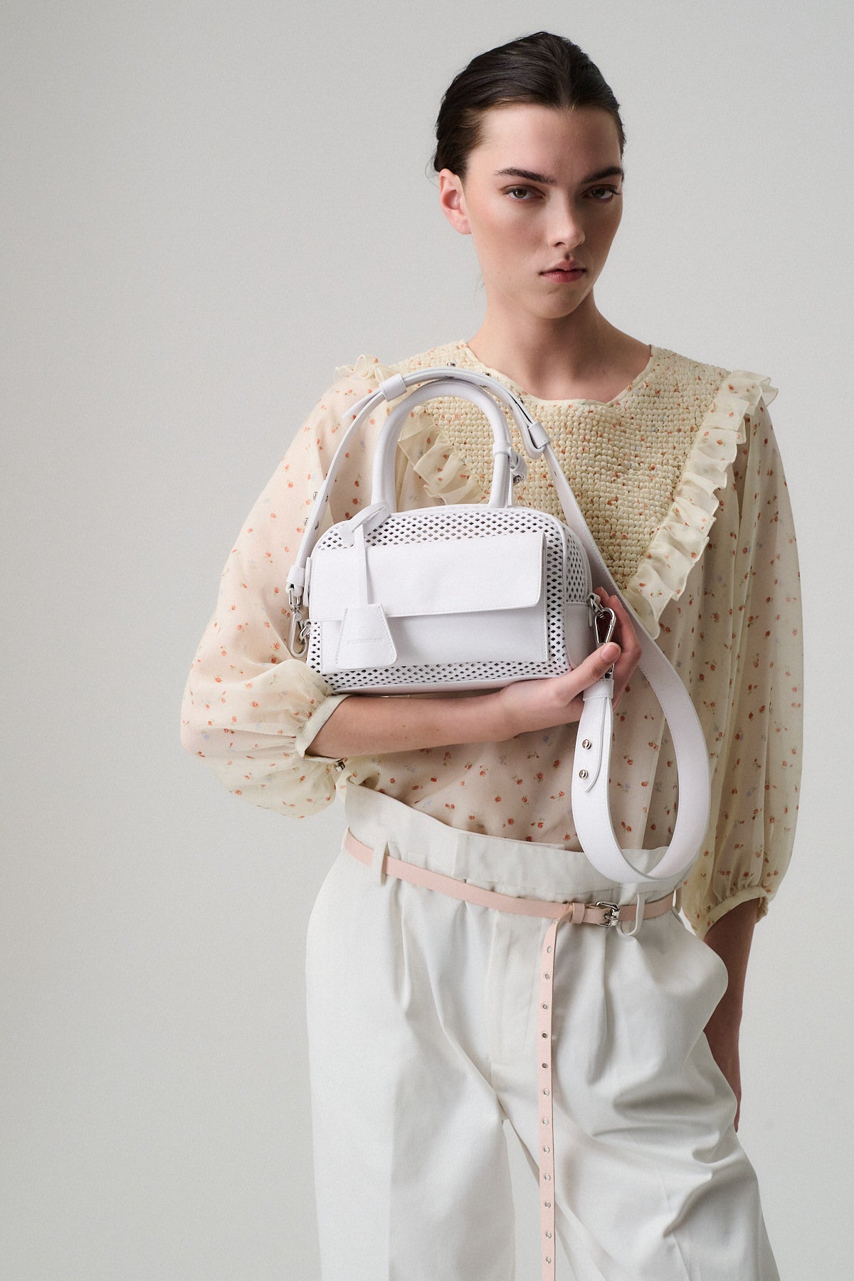 Donna con borsa ZOE MINI VITELLO FORATO, indossa una blusa chiara con dettagli e pantaloni bianchi, stile elegante.