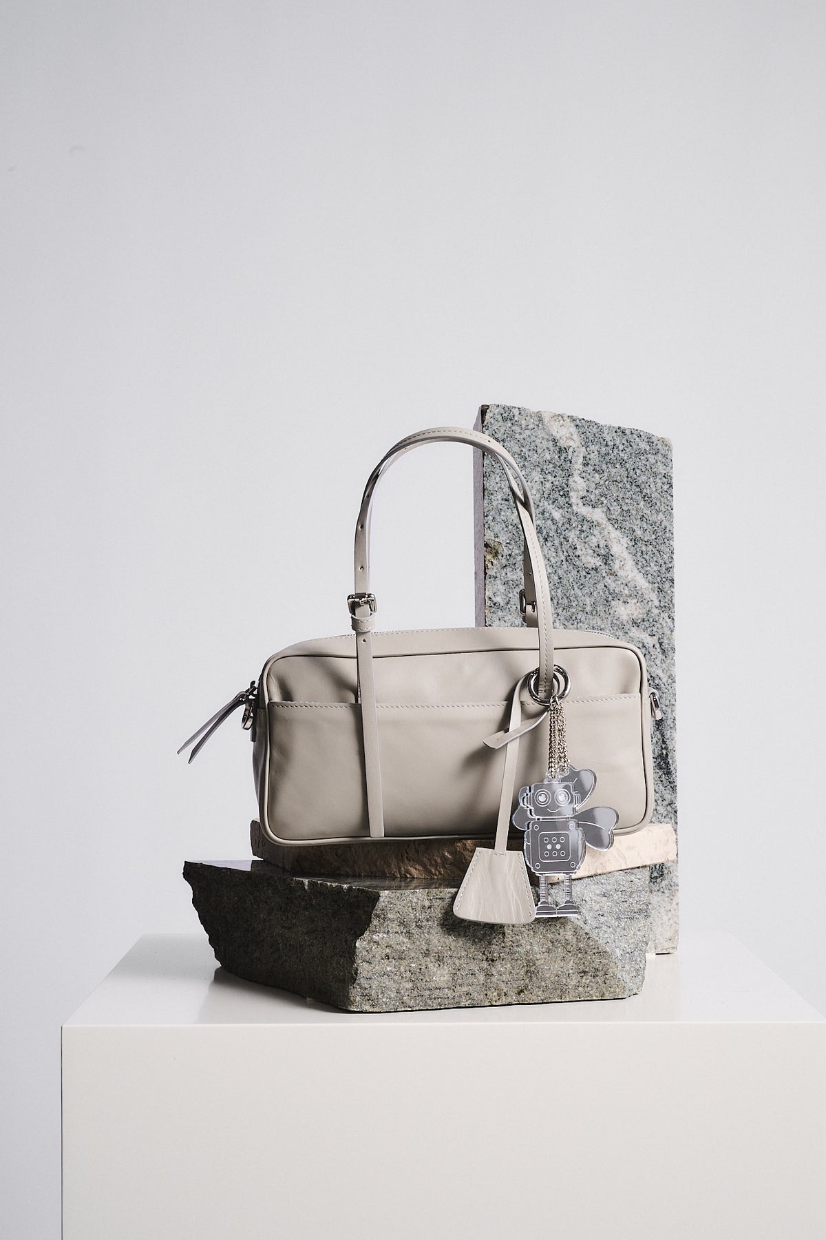 CHARMS PLEXI LIBELLULA attached to a stylish beige bag displayed on stone, showcasing a modern accessory.