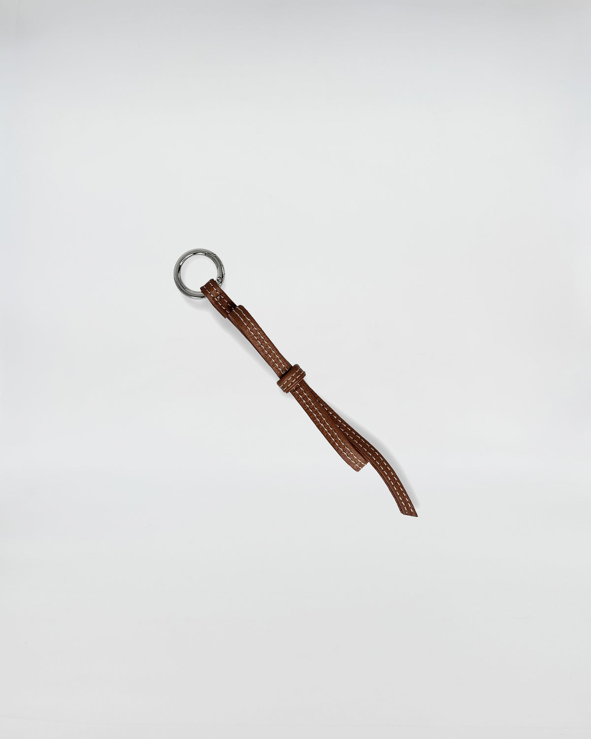 CHARMS IN PELLE FIOCCO in brown leather with a metallic ring, adding a playful touch to accessories.