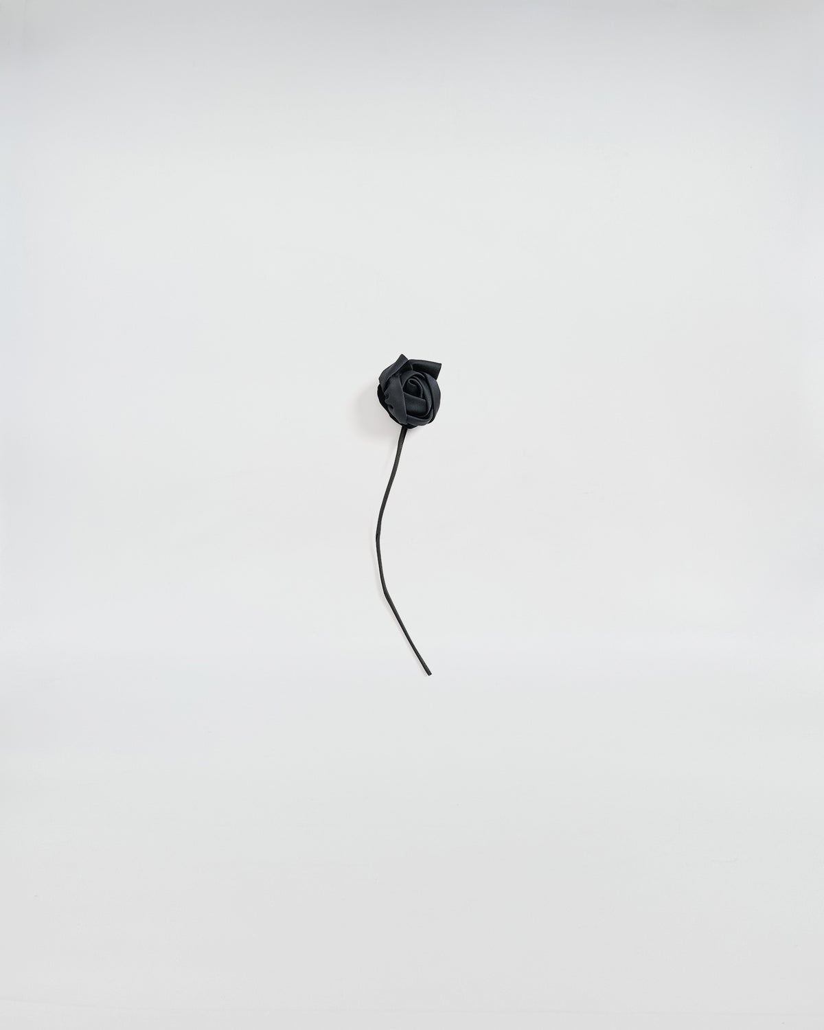 Elegant black satin rose brooch with a delicate stem on a light background.