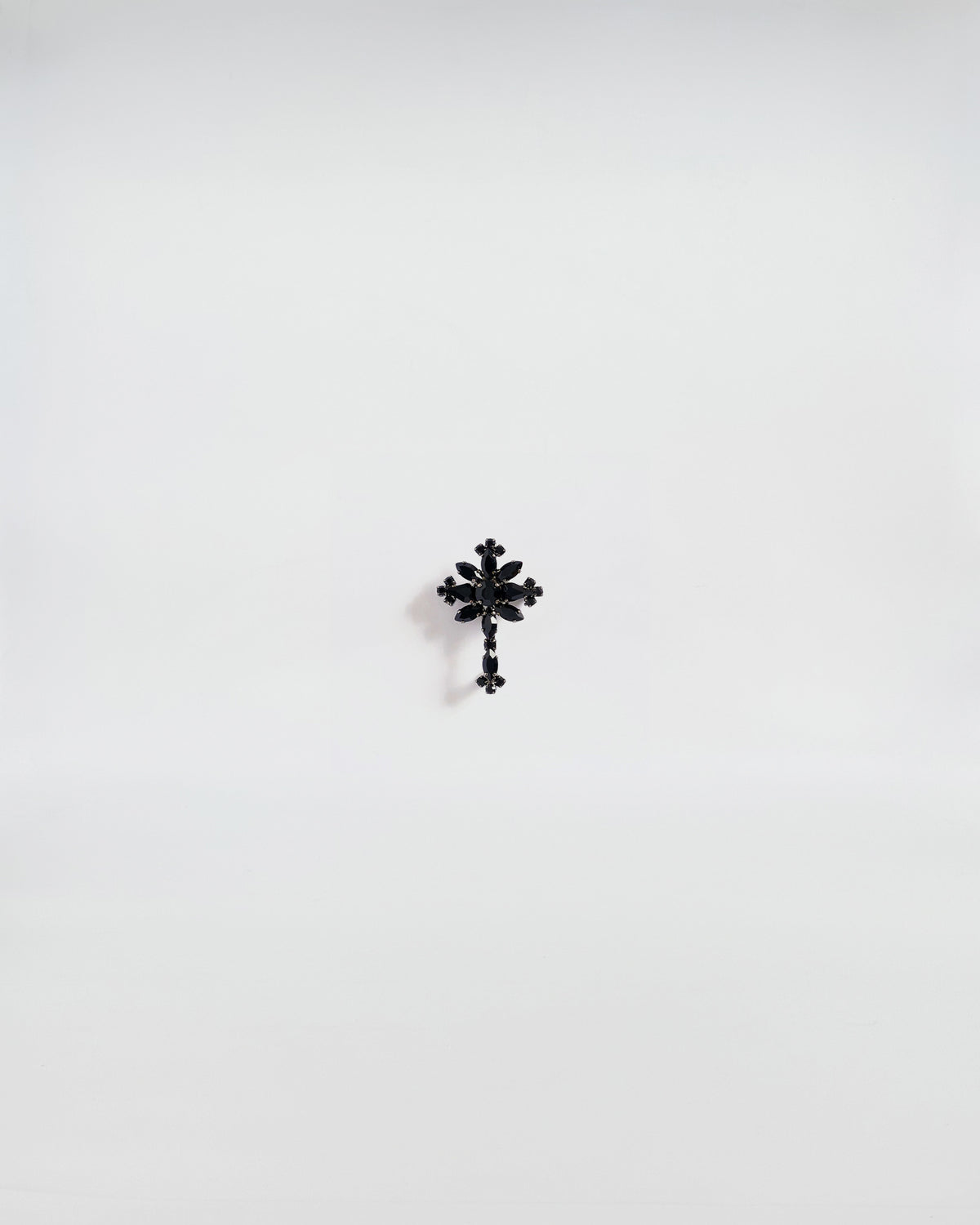 SPILLA IN STRASS CROCE, brooch with black stone and gunmetal finish on a white background.