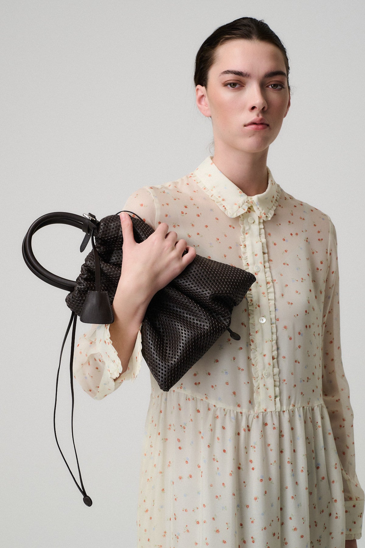 Modella in abito chiaro che mostra la borsa OLLY VITELLO FORATO, elegante e con design moderno.