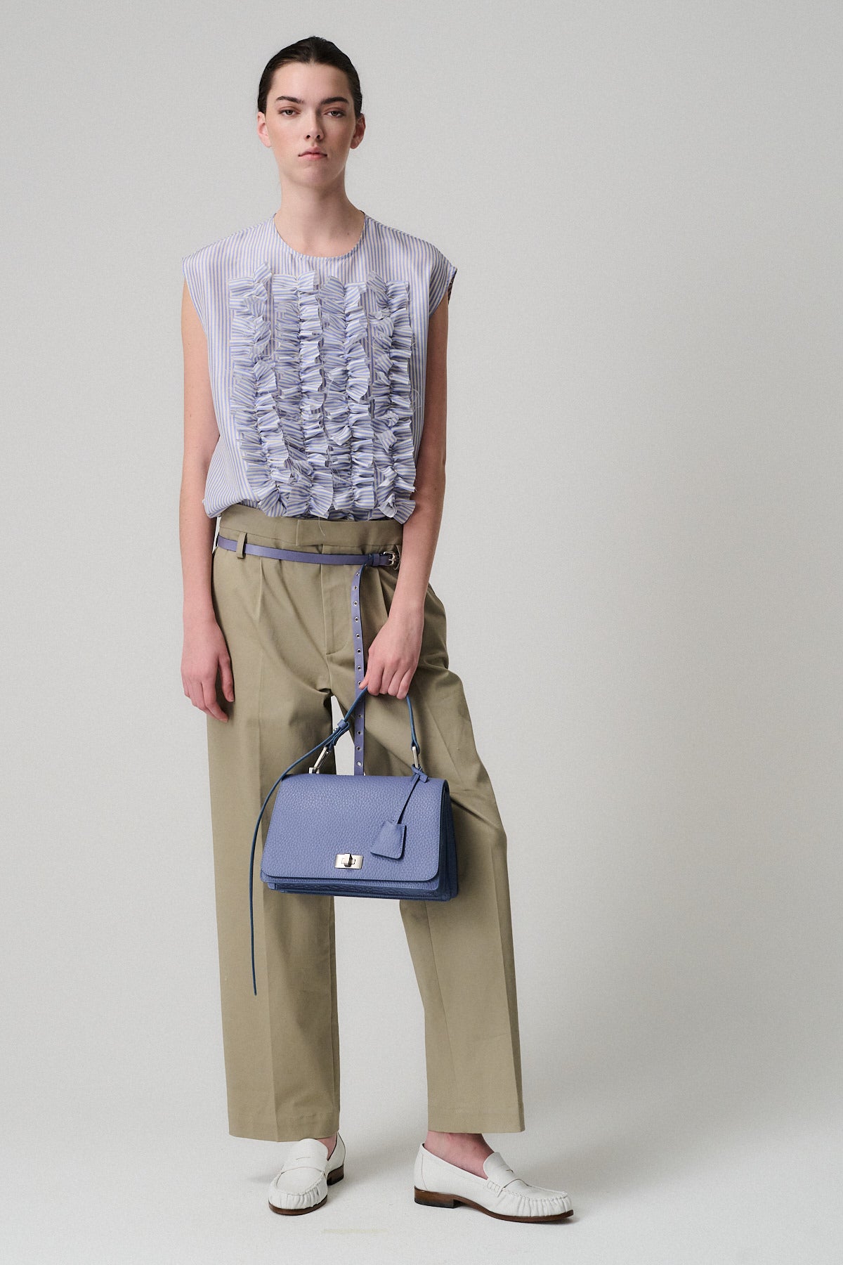 Immagine di un modello femminile con top grigio e pantaloni beige, che tiene la borsa QUEEN VITELLO.