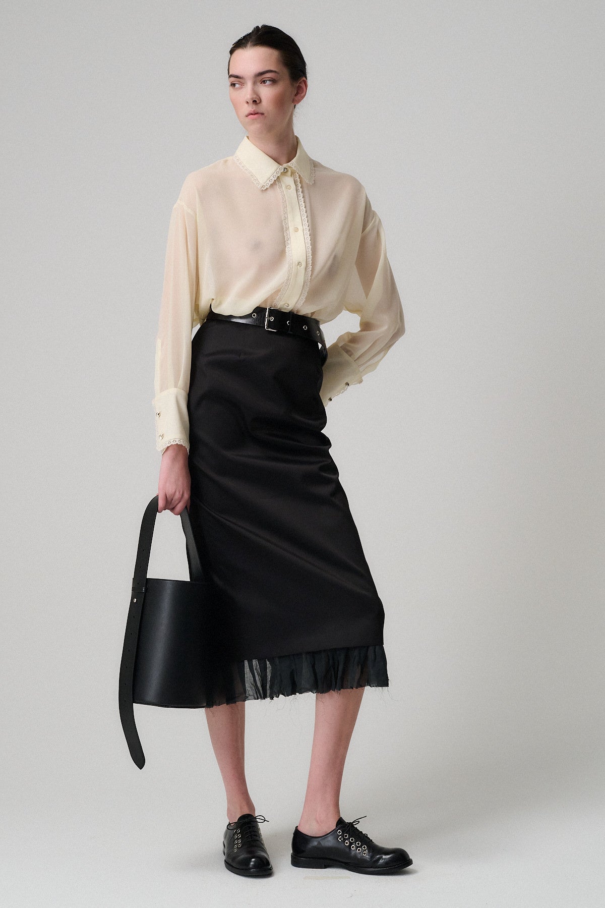 Modella con camicia chiara e gonna nera, tiene in mano una borsa Celeste Vitello Liscio, stile elegante e raffinato.