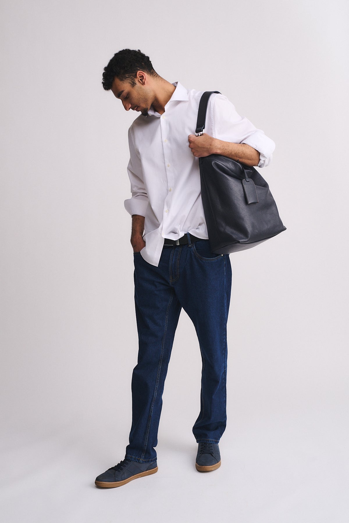 Uomo con borsa Ford personalizzata in pelle, indossando una camicia bianca e jeans, in pose eleganti.